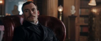 Movie still from “Enola Holmes” (2020), directed by Harry Bradbeer – A man sitting in a leather chair in a room; Close Up shot, Low angle