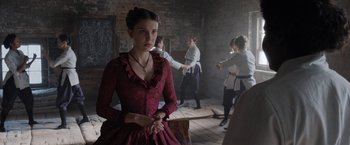 Movie still from “Enola Holmes” (2020), directed by Harry Bradbeer – A woman in a red dress standing in front of other women; Medium shot, Over the shoulder angle