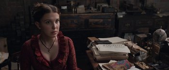 Movie still from “Enola Holmes” (2020), directed by Harry Bradbeer – A woman sitting in front of a stack of papers on top of a desk; Close Up shot, Over the shoulder angle
