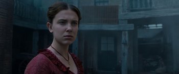 Movie still from “Enola Holmes” (2020), directed by Harry Bradbeer – A woman in a red dress standing in front of a building; Close Up shot, Over the shoulder angle