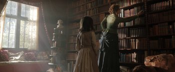Movie still from “Enola Holmes” (2020), directed by Harry Bradbeer – Two women in old - fashioned dresses in front of a book shelf; Medium shot, Low angle