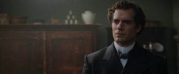 Movie still from “Enola Holmes” (2020), directed by Harry Bradbeer – A man wearing a suit and bow tie in front of a wooden cabinet; Close Up shot, Over the shoulder angle