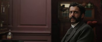 Movie still from “Enola Holmes” (2020), directed by Harry Bradbeer – A man in a suit and tie in front of a wall; Close Up shot, Low angle