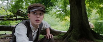 Movie still from “Enola Holmes” (2020), directed by Harry Bradbeer – A young woman in a hat and vest leaning against a tree; Close Up shot, Low angle
