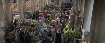 Movie still from “Enola Holmes” (2020), directed by Harry Bradbeer – A group of people standing around a market filled with lots of fresh produce; Extreme Wide shot, High angle