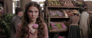 Movie still from “Enola Holmes” (2020), directed by Harry Bradbeer – A woman holding a pink flower in her hand; Close Up shot, Over the shoulder angle