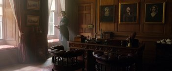 Movie still from “Enola Holmes” (2020), directed by Harry Bradbeer – A man in a suit standing in front of a window; Wide shot, Low angle