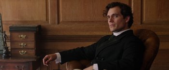 Movie still from “Enola Holmes” (2020), directed by Harry Bradbeer – A man sitting in a chair wearing a suit and tie; Close Up shot, Over the shoulder angle