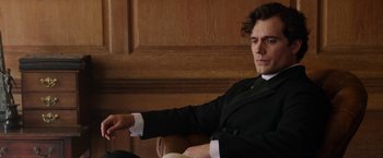 Movie still from “Enola Holmes” (2020), directed by Harry Bradbeer – A man sitting in a chair holding a remote control; Close Up shot, Over the shoulder angle