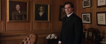 Movie still from “Enola Holmes” (2020), directed by Harry Bradbeer – A man standing in front of a portrait of a woman; Medium shot, Over the shoulder angle