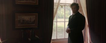 Movie still from “Enola Holmes” (2020), directed by Harry Bradbeer – A man standing in front of a large window; Medium shot, Over the shoulder angle
