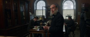 Movie still from “Enola Holmes” (2020), directed by Harry Bradbeer – A man with a long beard is sitting at a desk; Medium shot, Low angle