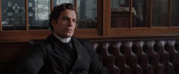 Movie still from “Enola Holmes” (2020), directed by Harry Bradbeer – A man sitting on top of a couch in a room; Medium shot, Over the shoulder angle