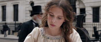 Movie still from “Enola Holmes” (2020), directed by Harry Bradbeer – A woman in a dress and a top hat looking down; Close Up shot, Low angle