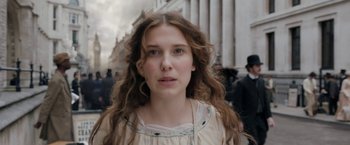 Movie still from “Enola Holmes” (2020), directed by Harry Bradbeer – A woman with long brown curly hair standing in front of a building; Close Up shot, Low angle