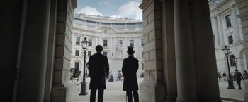 Movie still from “Enola Holmes” (2020), directed by Harry Bradbeer – Two men in top hats are standing in front of a building; Wide shot, Over the shoulder angle
