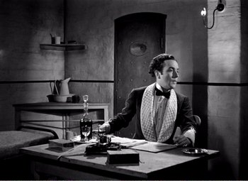 Movie still from “Kind Hearts and Coronets” (1949), directed by Robert Hamer – A black and white photo of a man sitting at a table; Medium shot, Low angle