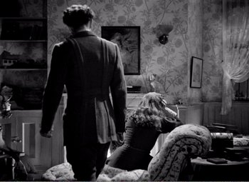 Movie still from “Kind Hearts and Coronets” (1949), directed by Robert Hamer – A man and a woman are standing in a living room; Wide shot, High angle