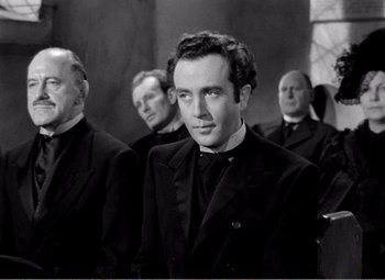 Movie still from “Kind Hearts and Coronets” (1949), directed by Robert Hamer – A group of men standing next to each other in suits; Medium shot, Over the shoulder angle