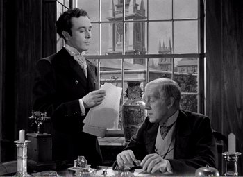 Movie still from “Kind Hearts and Coronets” (1949), directed by Robert Hamer – A man standing next to another man at a table; Medium shot, Over the shoulder angle