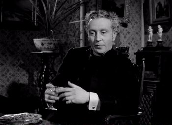 Movie still from “Kind Hearts and Coronets” (1949), directed by Robert Hamer – A man sitting at a table with a glass of wine in front of him; Medium shot, High angle