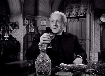 Movie still from “Kind Hearts and Coronets” (1949), directed by Robert Hamer – An older man sitting at a dinner table holding a wine glass; Medium shot, Low angle