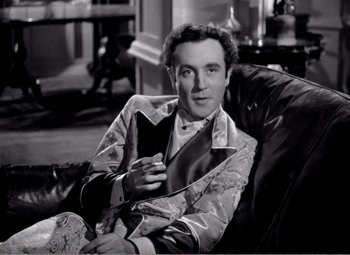 Movie still from “Kind Hearts and Coronets” (1949), directed by Robert Hamer – A black and white photo of a man sitting in a chair holding a cell phone; Medium shot, High angle