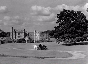 Movie still from “Kind Hearts and Coronets” (1949), directed by Robert Hamer – A man riding a horse drawn carriage down the middle of a road; Extreme Wide shot, High angle