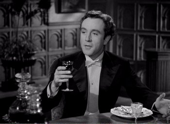 Movie still from “Kind Hearts and Coronets” (1949), directed by Robert Hamer – A man sitting at a table holding a glass of wine; Medium shot, High angle