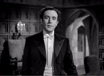 Movie still from “Kind Hearts and Coronets” (1949), directed by Robert Hamer – A man in a tuxedo standing next to a table; Medium shot, Low angle