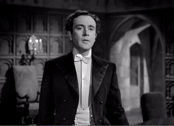 Movie still from “Kind Hearts and Coronets” (1949), directed by Robert Hamer – A man in a suit and bow tie standing in front of a building; Medium shot, Low angle