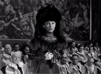 Movie still from “Kind Hearts and Coronets” (1949), directed by Robert Hamer – A woman in a black and white photo standing in front of a group of people; Medium shot, High angle