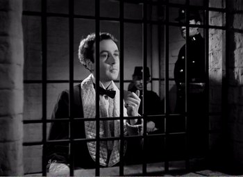 Movie still from “Kind Hearts and Coronets” (1949), directed by Robert Hamer – A man sitting in front of another man in a jail cell; Medium shot, Low angle