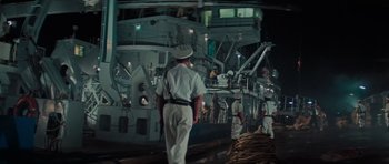 Movie still from “King Kong” (1976), directed by John Guillermin – A group of men standing next to each other near a boat; Wide shot, High angle