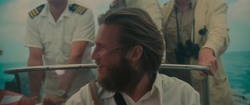 Movie still from “King Kong” (1976), directed by John Guillermin – A man with long hair and a goatee is smiling; Close Up shot, Over the shoulder angle