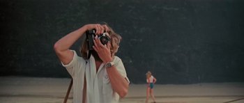 Movie still from “King Kong” (1976), directed by John Guillermin – A man taking a picture of a woman on the beach; Medium shot, Low angle