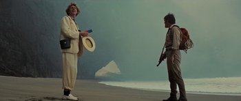 Movie still from “King Kong” (1976), directed by John Guillermin – Two men standing on the beach one is holding a gun and the other is wearing a hat; Wide shot, Low angle