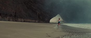 Movie still from “King Kong” (1976), directed by John Guillermin – A woman running on the beach near a cave; Extreme Wide shot, High angle