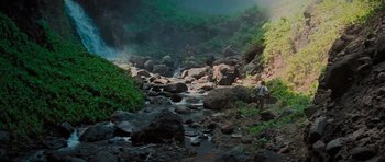 Movie still from “King Kong” (1976), directed by John Guillermin – A man standing on a rocky hillside near a river; Extreme Wide shot, High angle