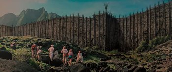 Movie still from “King Kong” (1976), directed by John Guillermin – A group of people standing next to each other near a wooden fence; Extreme Wide shot, Low angle