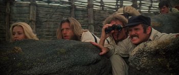 Movie still from “King Kong” (1976), directed by John Guillermin – Two people looking through binoculars while standing next to a rock; Close Up shot, Low angle