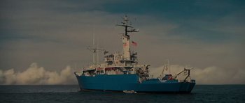 Movie still from “King Kong” (1976), directed by John Guillermin – A large blue boat in the water with a flag on it's mast; Extreme Wide shot, Low angle