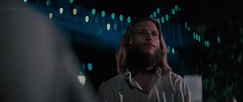 Movie still from “King Kong” (1976), directed by John Guillermin – A man with long hair and a beard is standing in front of lights; Close Up shot, Low angle