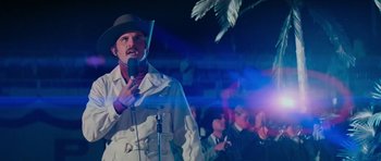 Movie still from “King Kong” (1976), directed by John Guillermin – A man with a microphone in front of a group of people; Medium shot, Low angle