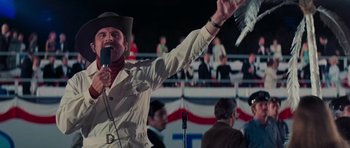 Movie still from “King Kong” (1976), directed by John Guillermin – A man holding a microphone up in the air while standing in front of an audience; Medium shot, Low angle