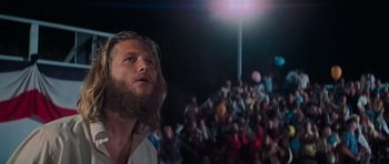 Movie still from “King Kong” (1976), directed by John Guillermin – A crowd of people watching a bearded man; Medium shot, Low angle