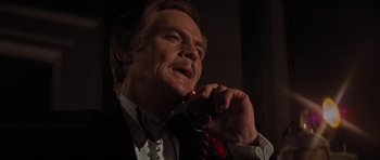 Movie still from “King Kong” (1976), directed by John Guillermin – An older man talking on a phone while wearing a suit and tie; Close Up shot, Low angle