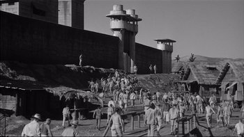 Movie still from “King Rat” (1965), directed by Bryan Forbes – A black - and - white photo of a group of people standing around; Extreme Wide shot, High angle