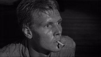 Movie still from “King Rat” (1965), directed by Bryan Forbes – A young man smoking a cigarette while sitting on a couch; Close Up shot, Low angle