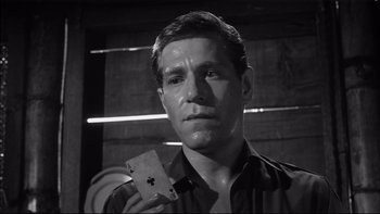 Movie still from “King Rat” (1965), directed by Bryan Forbes – A black and white photo of a man holding a playing card; Close Up shot, Low angle